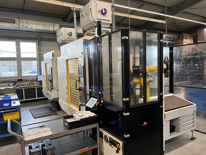 Fertigungszelle, in der black4st®-Teile entstehen: Ein FANUC-Roboter beschickt das Bearbeitungszentrum hinter Sicherheitsverglasung